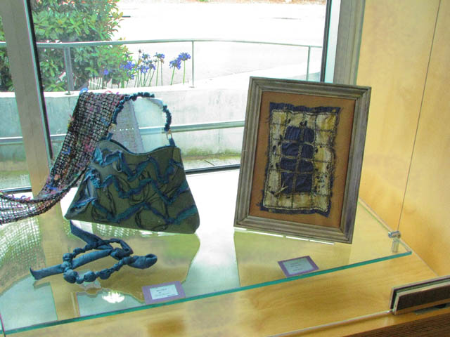 A display case containing a green handbag decorated with blue wavy ruffles