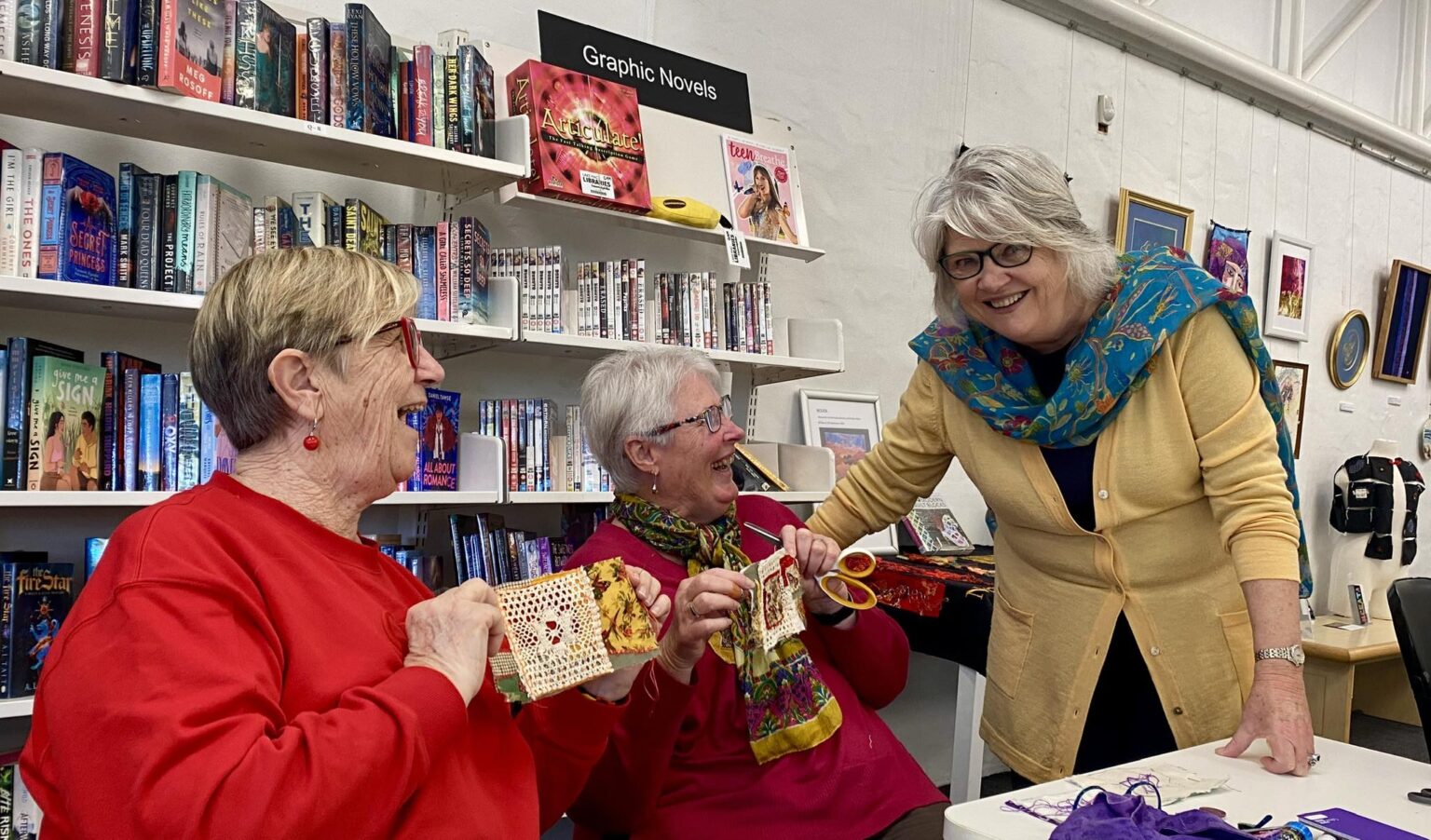 Three older women laughing together in a library setting